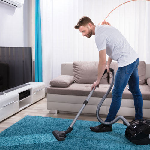 Man vacuuming his living room with bright blue carpet. 